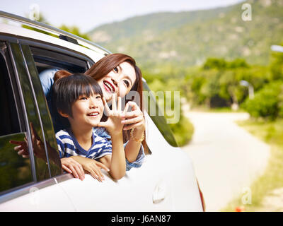 happy asian mother and son sticking heads out of rear window of a car looking at scenery. Stock Photo