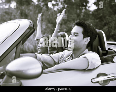 young asian couple riding in a convertible sport car enjoying the cool breeze at sunset, black and white. Stock Photo