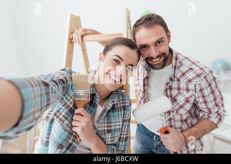 Creative young couple renovating their house and painting walls, they are taking a self portrait together and smiling at camera Stock Photo