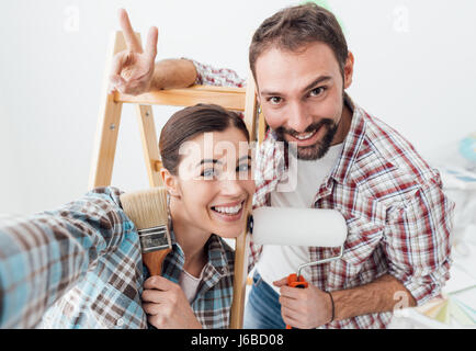 Creative young couple renovating their house and painting walls, they are taking a self portrait together and smiling at camera Stock Photo