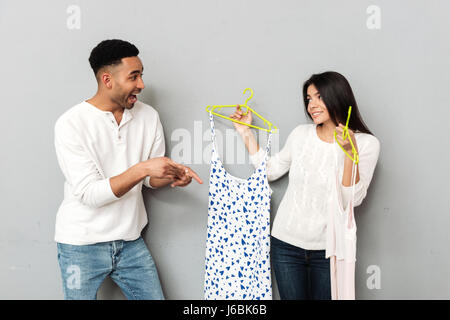 Young cheerful man choosing between two woman's dresses isolated Stock Photo