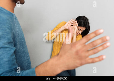 Woman hiding because of afraid of her agressive husband isolated over grey background Stock Photo