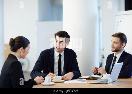 Young specialist answering questions of two employers during interview Stock Photo