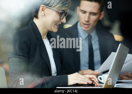 Side view portrait of young creative businesswoman using laptop in work meeting with colleagues Stock Photo