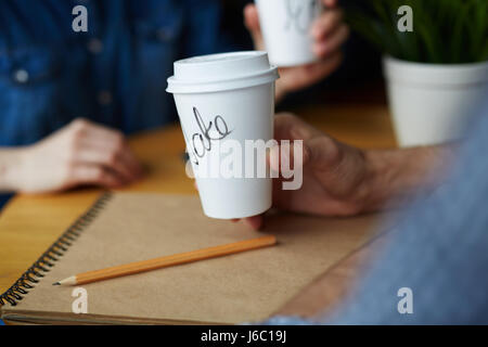 Closeup shot of two paper coffee cups with names on them in hands of young people working in cafe Stock Photo