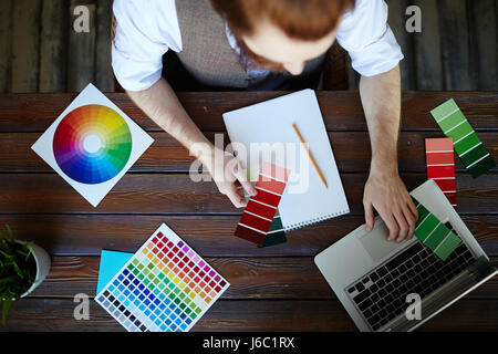 Directly above view portrait of creative designer working in modern studio, choosing color scheme from swatches and using laptop Stock Photo