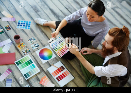 High angle view of creative designers team, man and woman,  working in modern studio sitting on wooden floor and  discussing projects color scheme Stock Photo