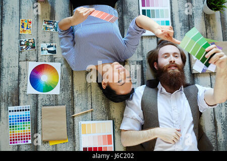 Directly above view of creative designers team , Asian woman and bearded man, working in modern studio lying on wooden floor and  discussing projects  Stock Photo