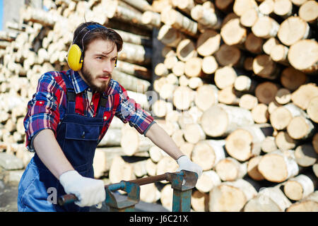 Portrait of man wearing earmuffs working on timber cutting site, transporting wood logs