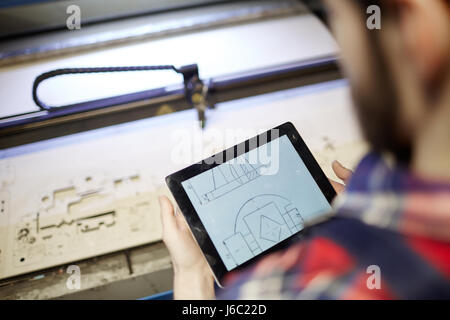 High angle shot of factory worker using digital tablet to operate laser cutting machine in workshop Stock Photo