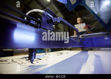 Closeup shot of laser cutting machine working in factory with blurred worker operating it in background Stock Photo
