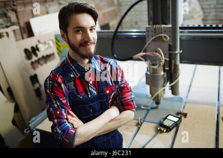 Portrait of handsome factory worker posing in workshop with machines and smiling to camera Stock Photo