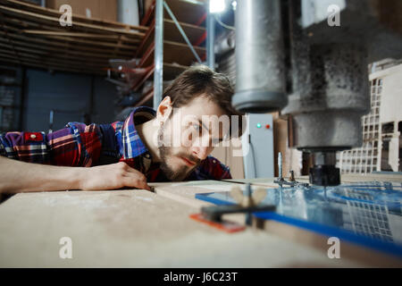 Portrait of handsome young engineer operating glass cutting machine, watching engraving process closely Stock Photo
