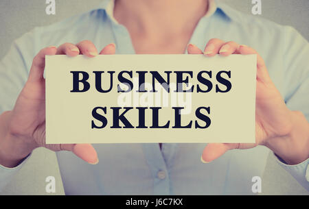 Closeup businesswoman hands holding white card sign with business skills text message isolated on grey wall office background. Retro instagram style i Stock Photo