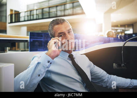 Confident mature businessman sitting and thinking in office while having phone conversation. Stock Photo