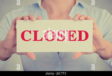 Closeup businesswoman hands holding white card sign with closed text message isolated on grey wall office background. Retro instagram style image Stock Photo
