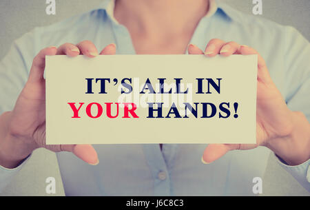 Image of businesswoman hands holding white card with It's All in Your hands! Motivating message sign isolated on grey wall office background. Stock Photo