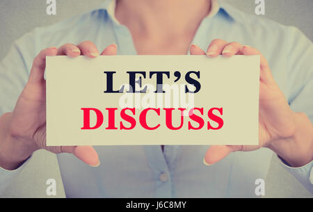 Businesswoman hands holding white card sign with let's discuss text message isolated on grey wall office background. Retro instagram style image Stock Photo