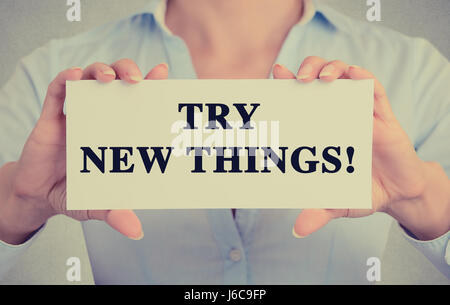 Closeup businesswoman hands holding white card sign with try new things text message isolated on grey wall office background. Retro instagram style im Stock Photo