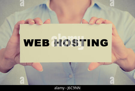 Business woman hands holding white card sign with web hosting text message isolated on grey wall office background. Retro instagram style image. Techn Stock Photo