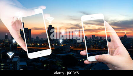Internet of things , iot , smart home , smart city and network connect concept. Hands holding white phones and wifi icon with city sunset view. Stock Photo
