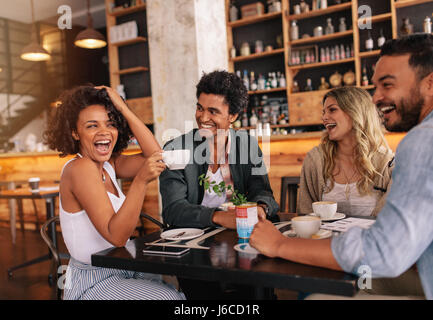 Happy young people sitting around cafe table and drinking coffee. Multiracial group of friends enjoying coffee together in a restaurant. Stock Photo