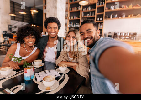 Happy young man taking selfie with friends in a cafe. Young multiracial people in a coffee shop making a self portrait. Stock Photo
