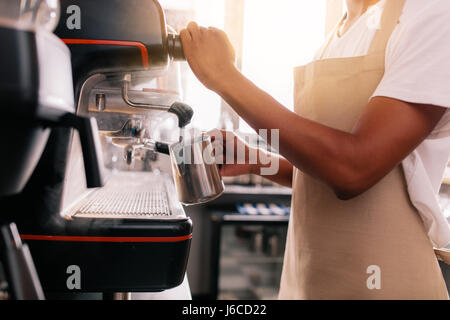 Close up of young man preparing coffee on machine. Barista holding metal jug warming milk using the coffee machine. Stock Photo