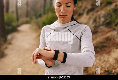 Asian female checking fitness progress on her smart watch. Fit young woman runner checking time on smart watch. Stock Photo