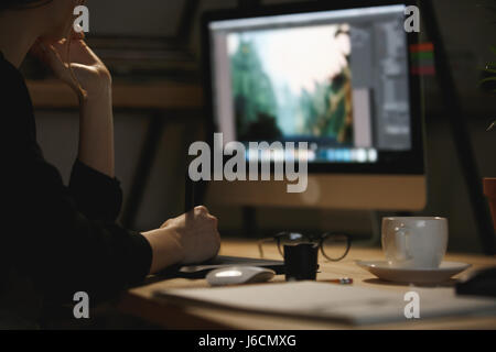 Cropped image of young lady designer sitting indoors at night using computer and graphics tablet. Stock Photo