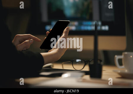 Cropped photo of young woman designer sitting indoors at night chatting by phone. Stock Photo