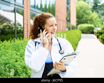 Closeup portrait, young smiling confident female doctor, healthcare professional talking on phone, giving consultation isolated background hospital ca Stock Photo