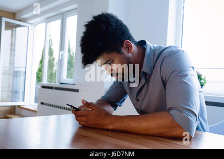 Happy bearded African businessman using phone at home at desk Stock Photo