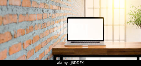 Blank screen laptop on wooden table red brick wall in sunrise background Stock Photo