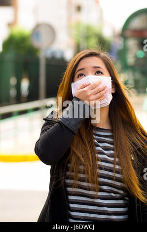 Young woman with his hand over the protective mask on the street in the city with air pollution, city background Stock Photo