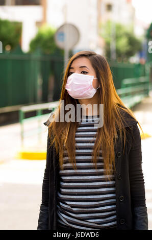 Young woman with protective mask on the street in the city with air pollution, city background Stock Photo