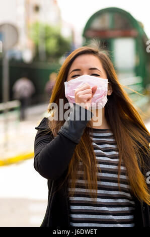 Young woman with protective mask feeling bad on the street in the city with air pollution, city background Stock Photo