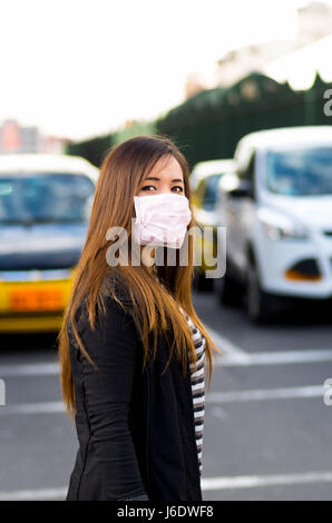 Young woman wearing protective mask on the street in the city with air pollution, traffic background Stock Photo