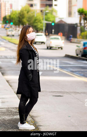 Young woman with protective mask posing on the street in the city with air pollution, city background Stock Photo