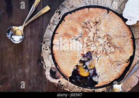 Above image of a blueberry and peach cobbler baked in a cast iron skillet over a rustic wood table top. Image shot from overhead. Perfect dessert for  Stock Photo
