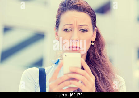 Upset stressed woman holding cellphone disgusted with message she received isolated corporate building background. Sad looking human face expression e