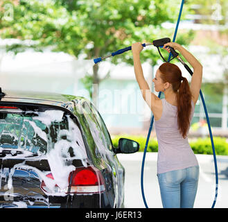 Picture, portrait young, smiling, happy, attractive woman washing automobile at manual car washing self service station, cleaning with foam, pressured Stock Photo