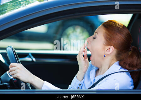 Closeup portrait sleepy, tired, fatigued, exhausted young attractive woman driving her car after long hour trip, isolated street traffic background. T Stock Photo