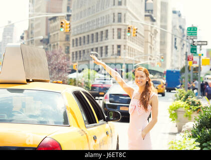 Attractive smiling woman in New York City. Beautiful happy summer shopper hailing for taxi cab outside with yellow taxi cab and Flatiron building in b Stock Photo