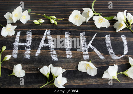 Word Haiku, Japanese Poetry, with Jasmine Flowers on a Rustic Wooden Background. Stock Photo
