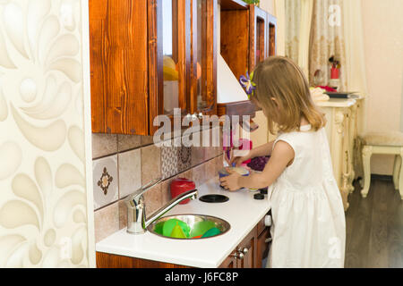 Active little preschool age child, cute toddler girl with blonde curly hair, shows playing kitchen, made of wood, plays in the kitchen Stock Photo