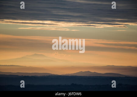 Mountains and hills in the middle of a golden, orange light during sunset, with a rooftop of clouds