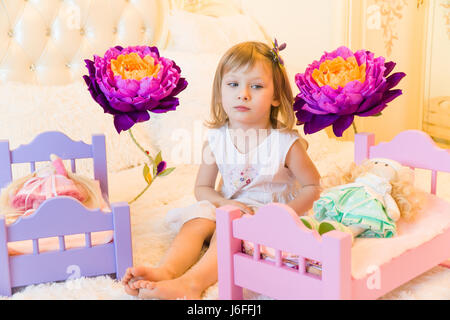 An active little preschool child, a pretty little girl with a blond curly hair, plays with her dolls, puts them to sleep in a steal Stock Photo