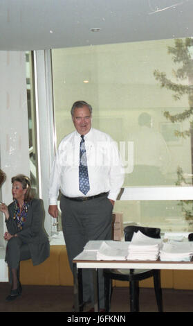 An individual stands next to a table with documents while another person is seated, indicating a discussion or administrative activity in a formal or operational setting. Stock Photo