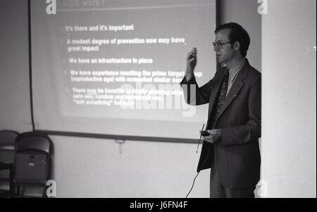 A man delivers a speech in front of a presentation screen, conveying information to an audience in a professional setting, emphasizing clarity, leadership, and engagement. Stock Photo